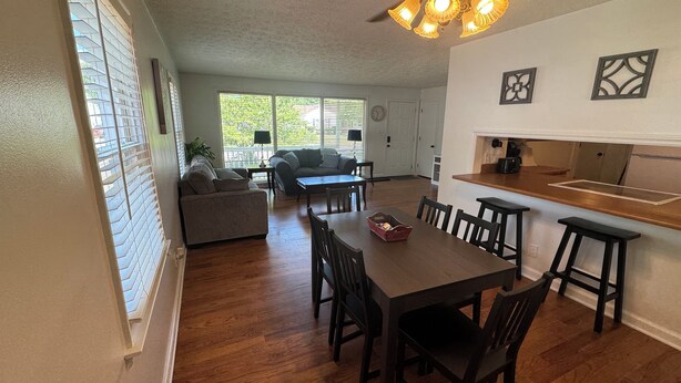 A dining area with a wooden table and chairs, a kitchen with a countertop and bar stools, and a living area with a sofa and a coffee table. - The Salon- 3 miles from WEC (Wilmington)