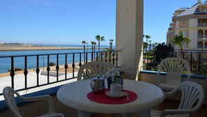 Un balcón con una mesa para dos, con vista a una playa y un cielo azul despejado.