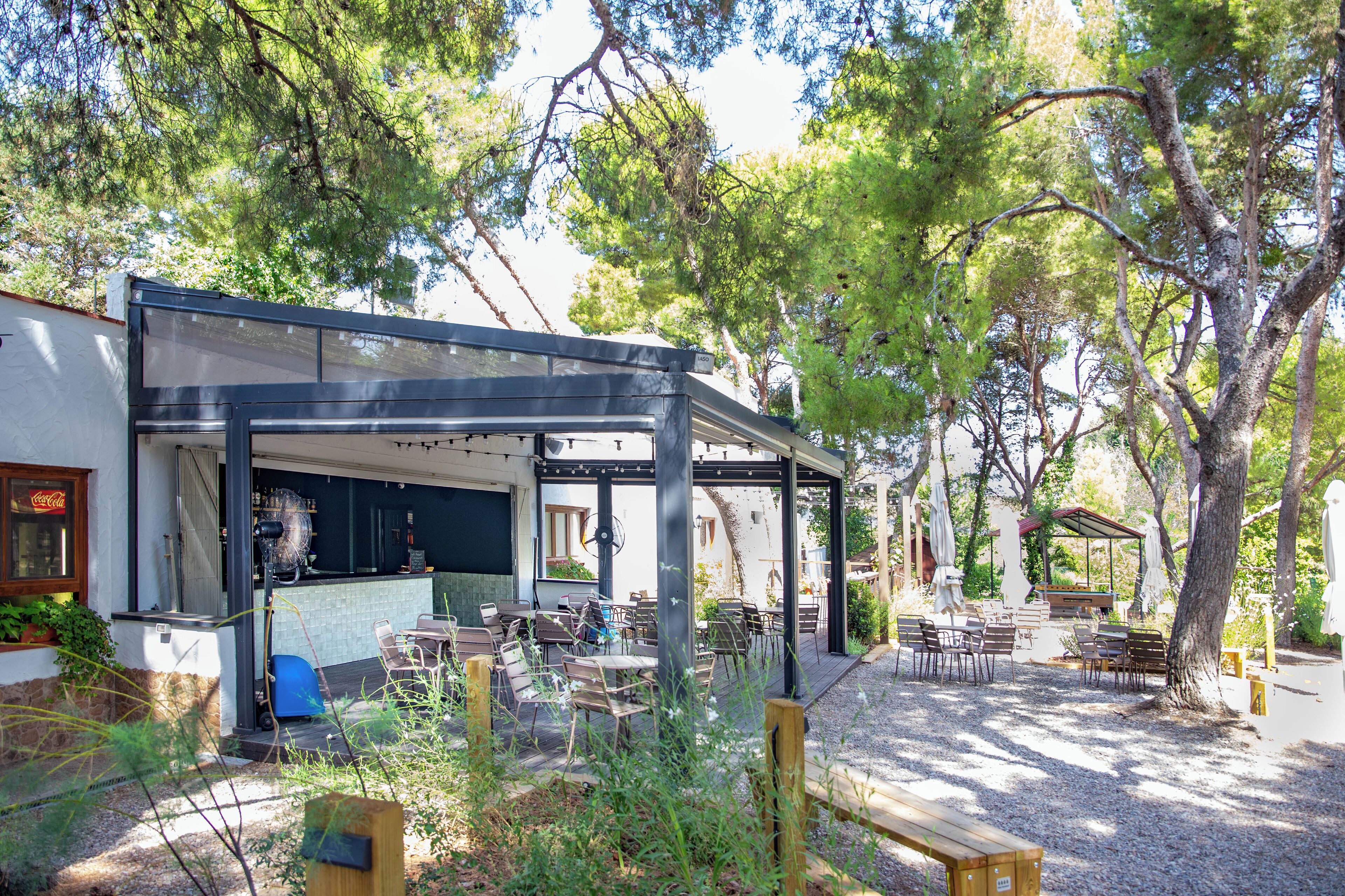An outdoor cafe with tables and chairs, a covered seating area, and a bar with a counter.