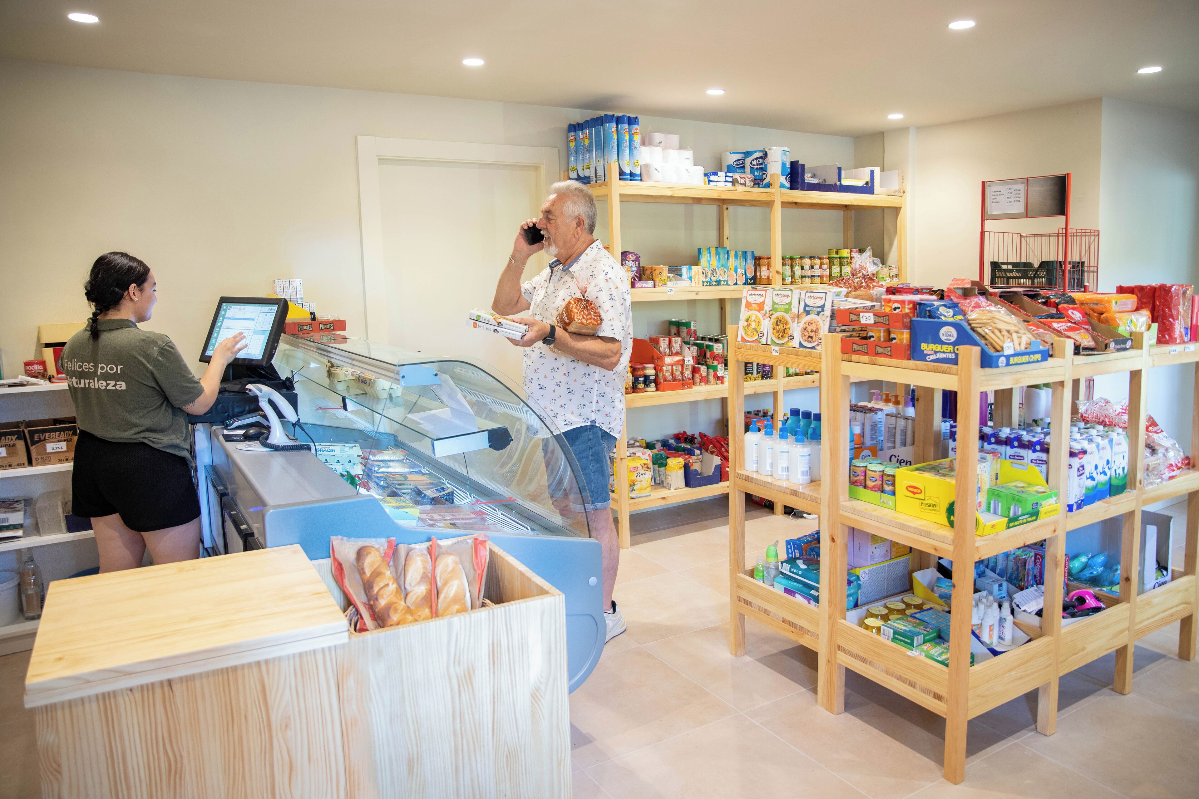 A bakery with a display case, shelves stocked with various baked goods, and a customer interacting with a cashier.