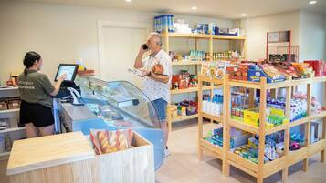 Una panadería con una vitrina, estantes llenos de productos horneados y un cliente interactuando con el cajero.