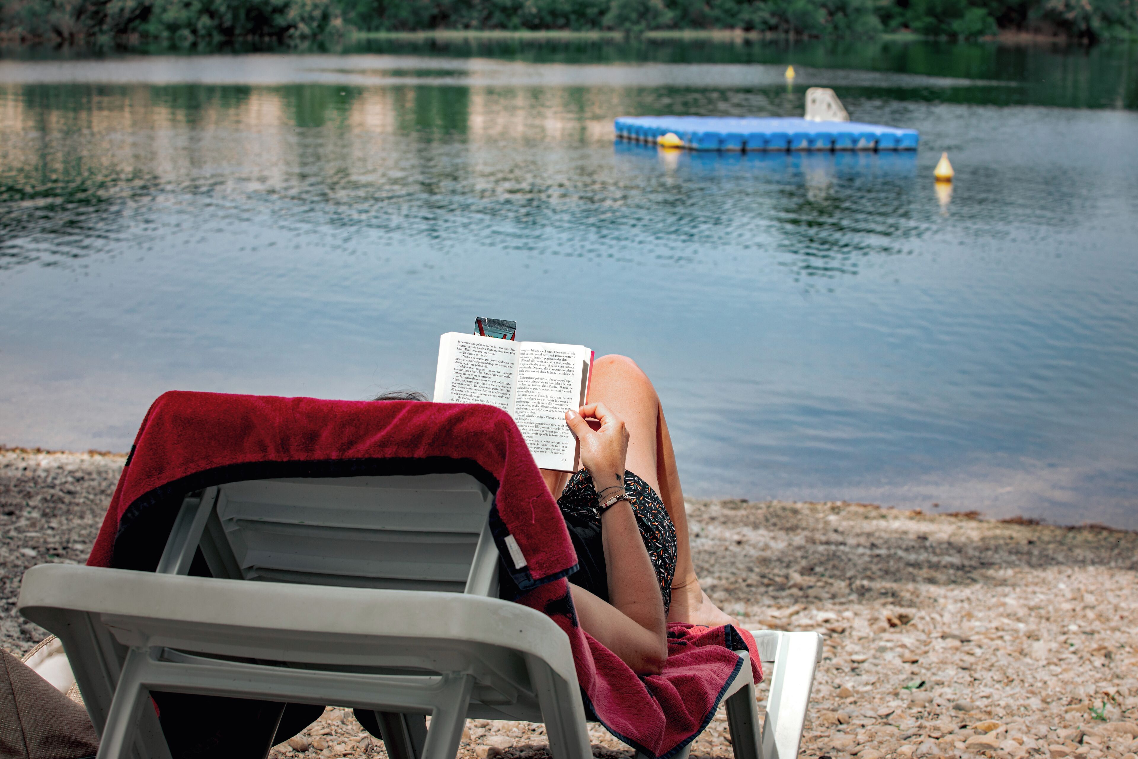 A person reading a book on a beach chair by a lake.