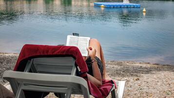 A person reading a book on a beach chair by a lake.
