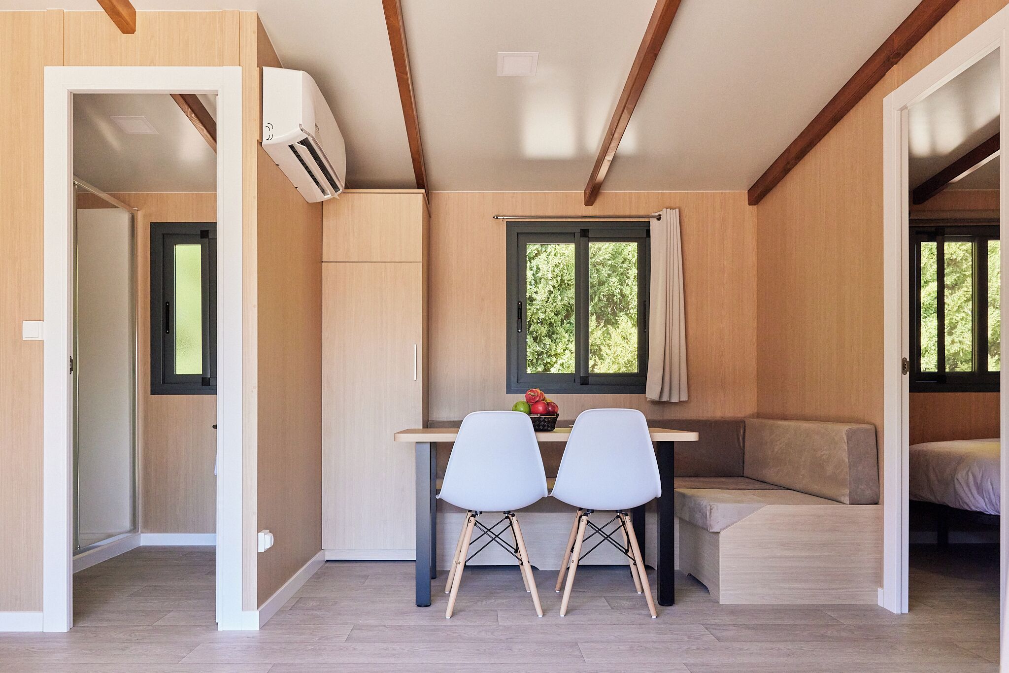 Een compacte kamer met een kitchenette, een eethoek met twee stoelen, een bankje en een raam met gordijnen.