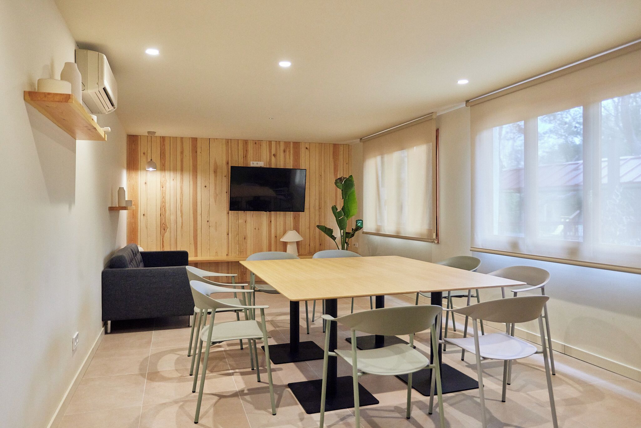 Una sala de reuniones moderna con un panel de pared de madera, un televisor de pantalla plana, una mesa grande y varias sillas.