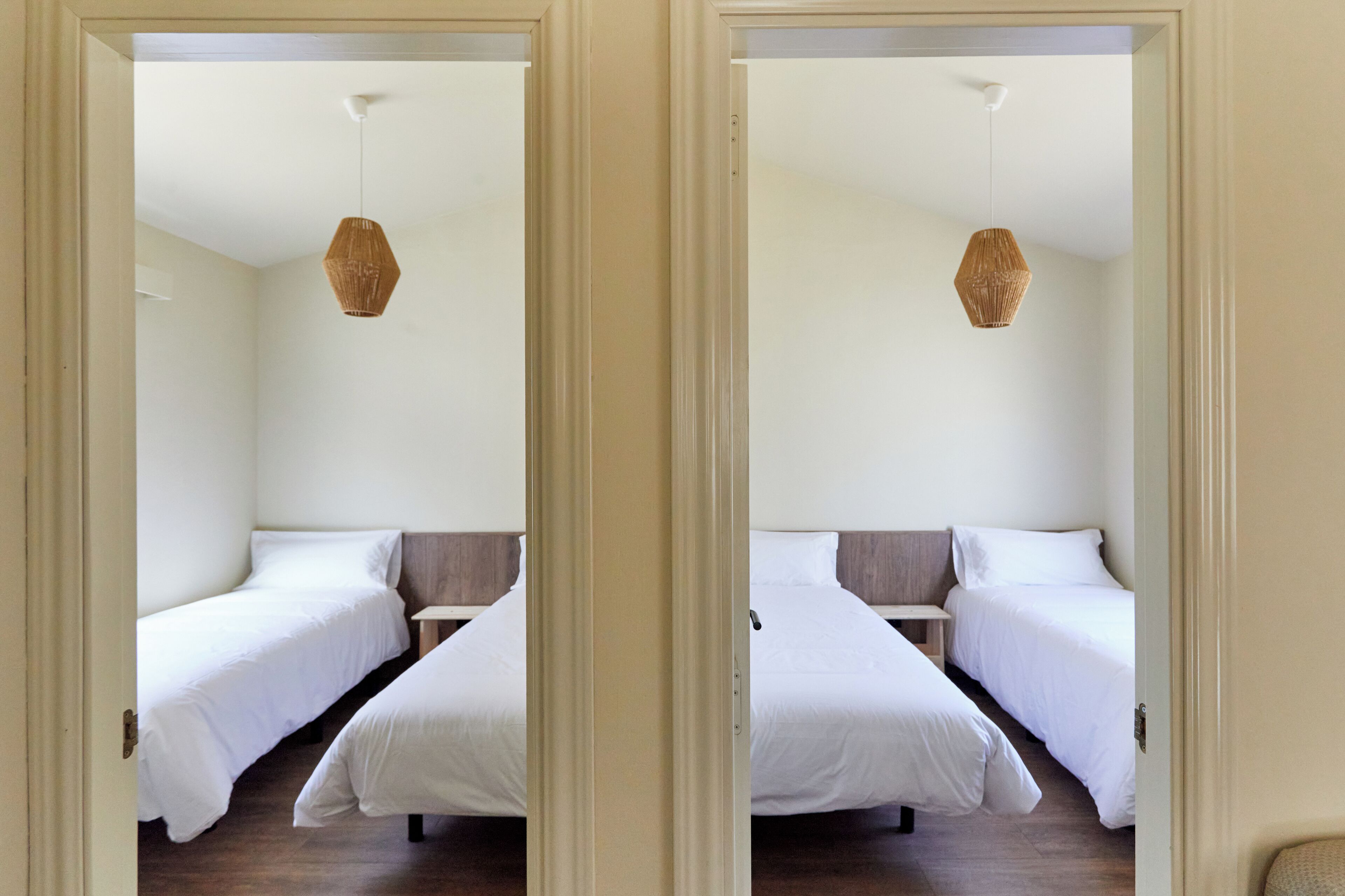 Una habitación con dos camas individuales, una mesita pequeña y una lámpara colgante.
