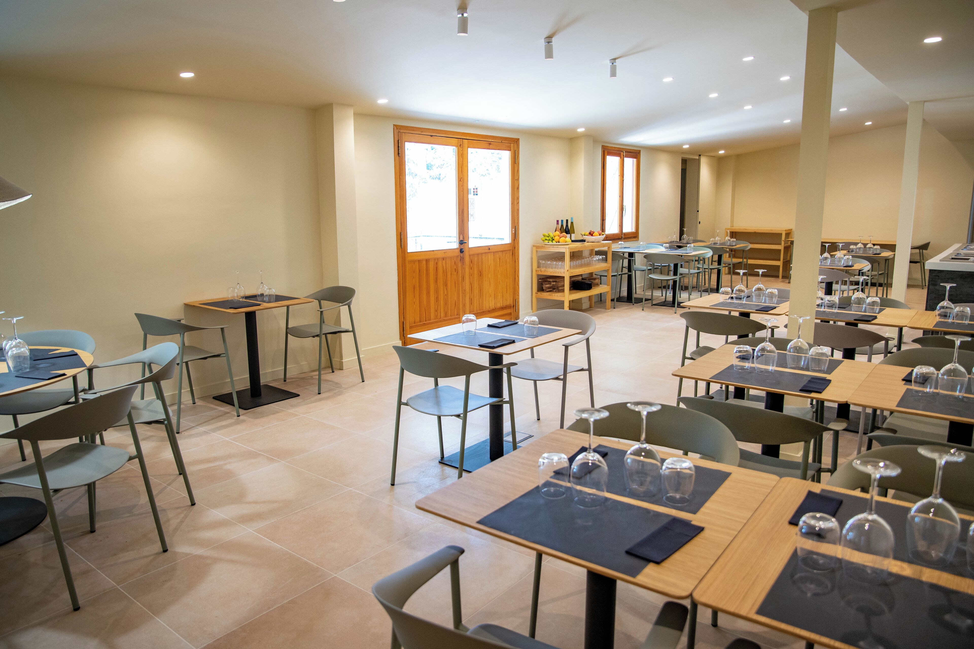 Un comedor amplio con varias mesas y sillas, puertas de madera y vistas al exterior.