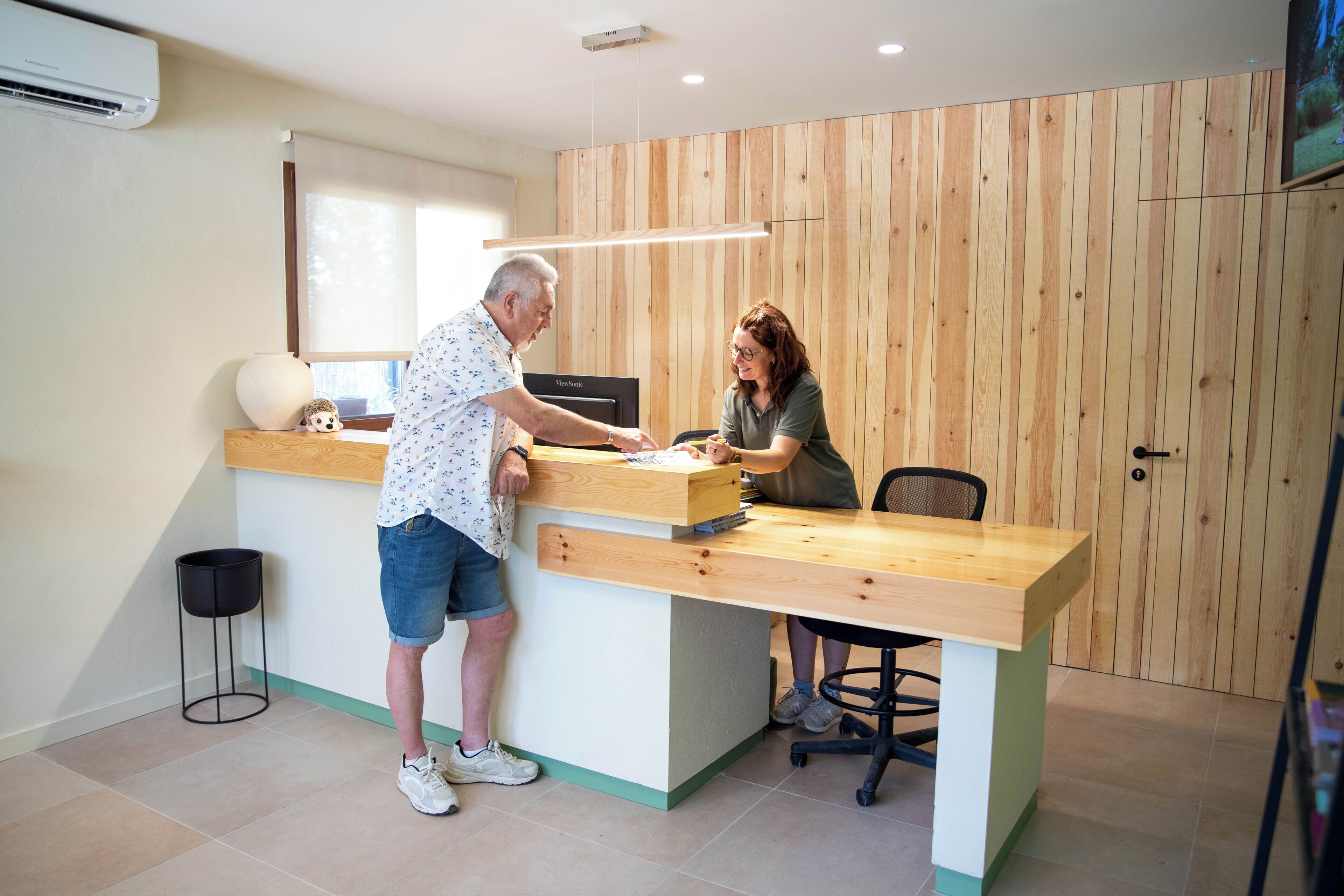 A reception desk with a wooden counter, a black office chair, and a small black stool.
