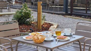 Un espace extérieur aménagé avec des tables et des chaises, un petit jardin et une terrasse couverte.
