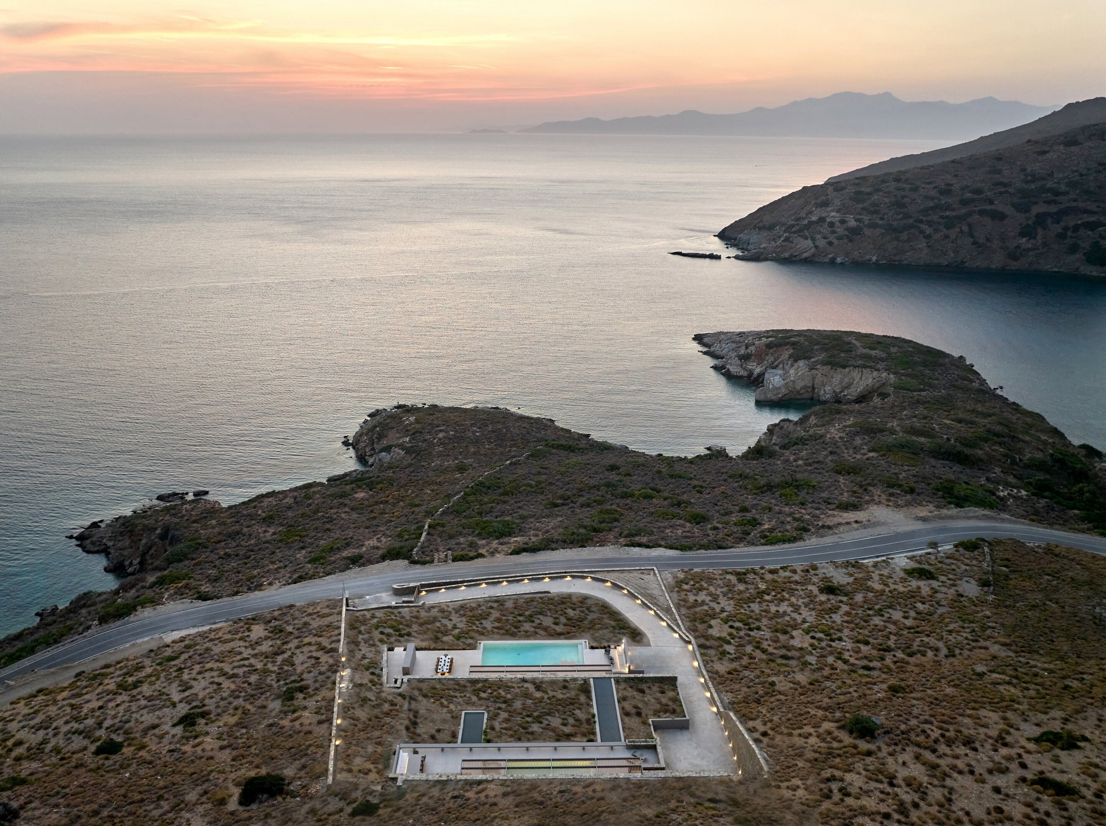 A coastal property with a swimming pool, a road, and a mountainous backdrop.