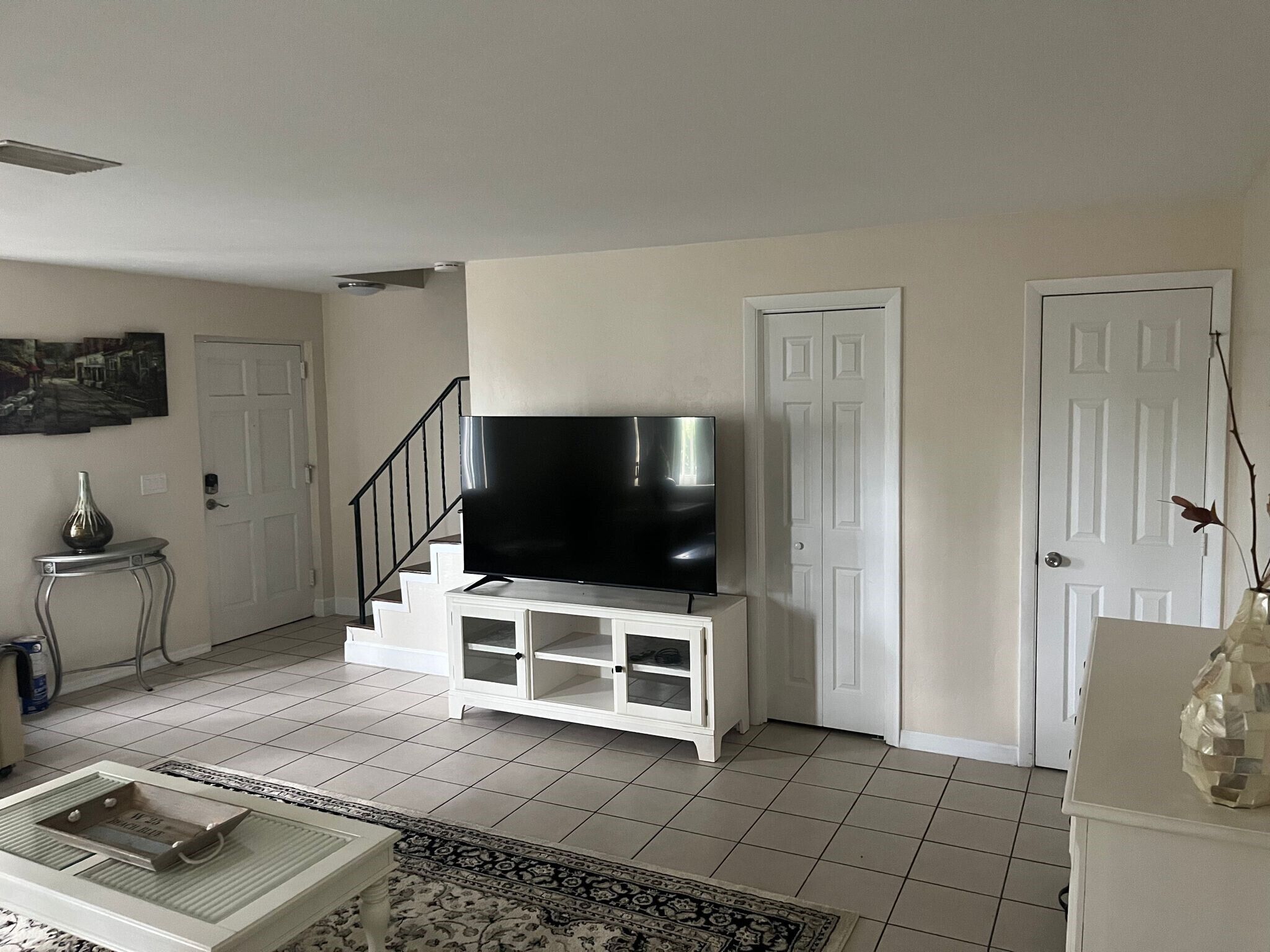 Un soggiorno con una televisione a schermo piatto su un mobile bianco, una scala e una porta.