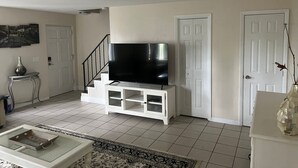 A living room with a flat-screen TV on a white entertainment unit, a staircase, and a door. - Cozy 2-bedroom apartment with AC and WiFi in welcoming Fort Myers (Fort Myers)