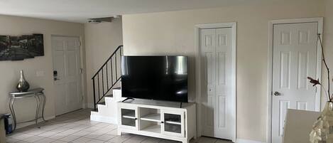 Un soggiorno con una televisione a schermo piatto su un mobile bianco, una scala e una porta.