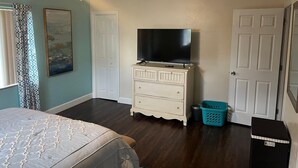 A bedroom with a bed, a dresser, a television, a ceiling fan, and a door. - Cozy 2-bedroom apartment with AC and WiFi in welcoming Fort Myers (Fort Myers)