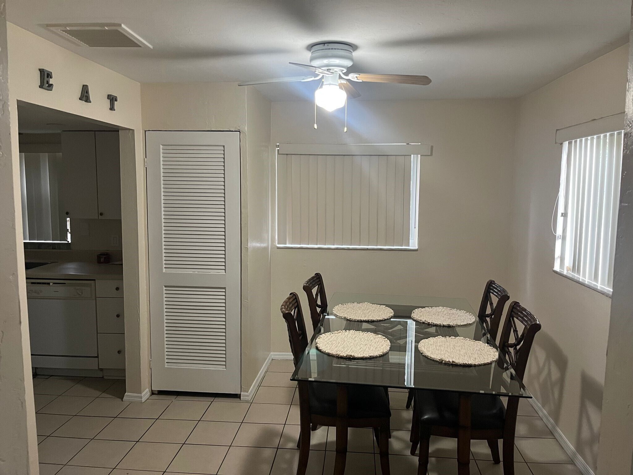 A dining area with a glass table, four chairs, and a ceiling fan.