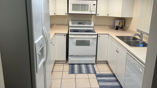A compact kitchen with white cabinets, a built-in microwave, a stove, and a sink. - Cozy 2-bedroom apartment with AC and WiFi in welcoming Fort Myers (Fort Myers)