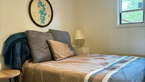 A bedroom with a bed, a map on the wall, a window, and a lamp.