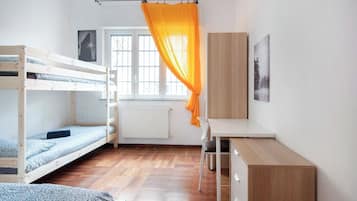 A dorm-style room with bunk beds, a desk, a chair, and a radiator.