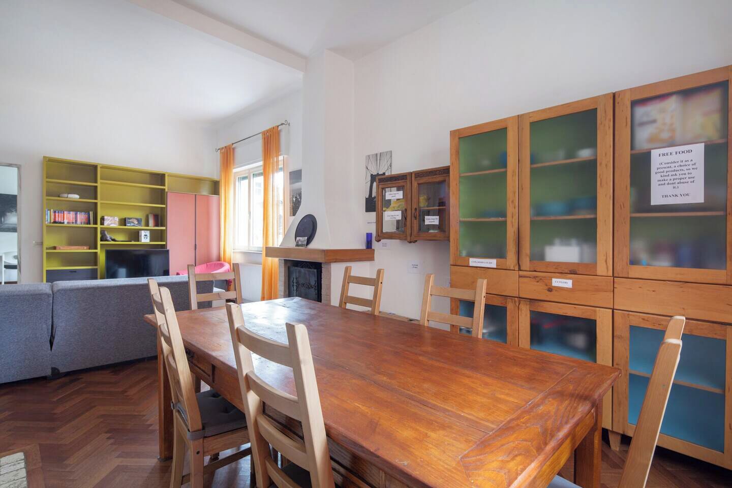 A dining area with a wooden table and chairs, a sofa, and a bookshelf.