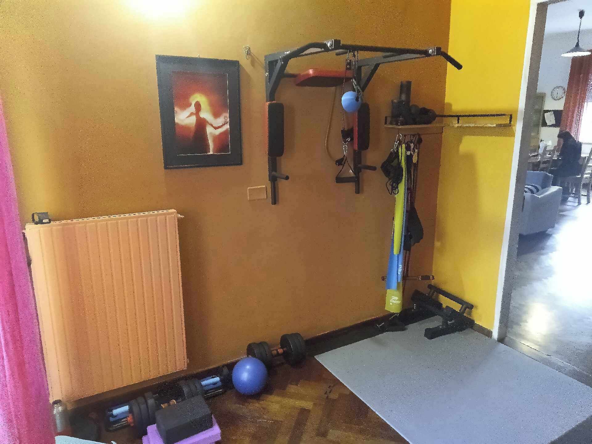 Une salle de sport à domicile équipée de matériel d’exercice, avec un radiateur et un tableau encadré accroché au mur.