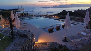 A pool area with lounge chairs and umbrellas, overlooking a body of water and distant land. - Cinque Terre breakfast home with optional access to Pool, Sauna and Jacuzzi (SARZANA)