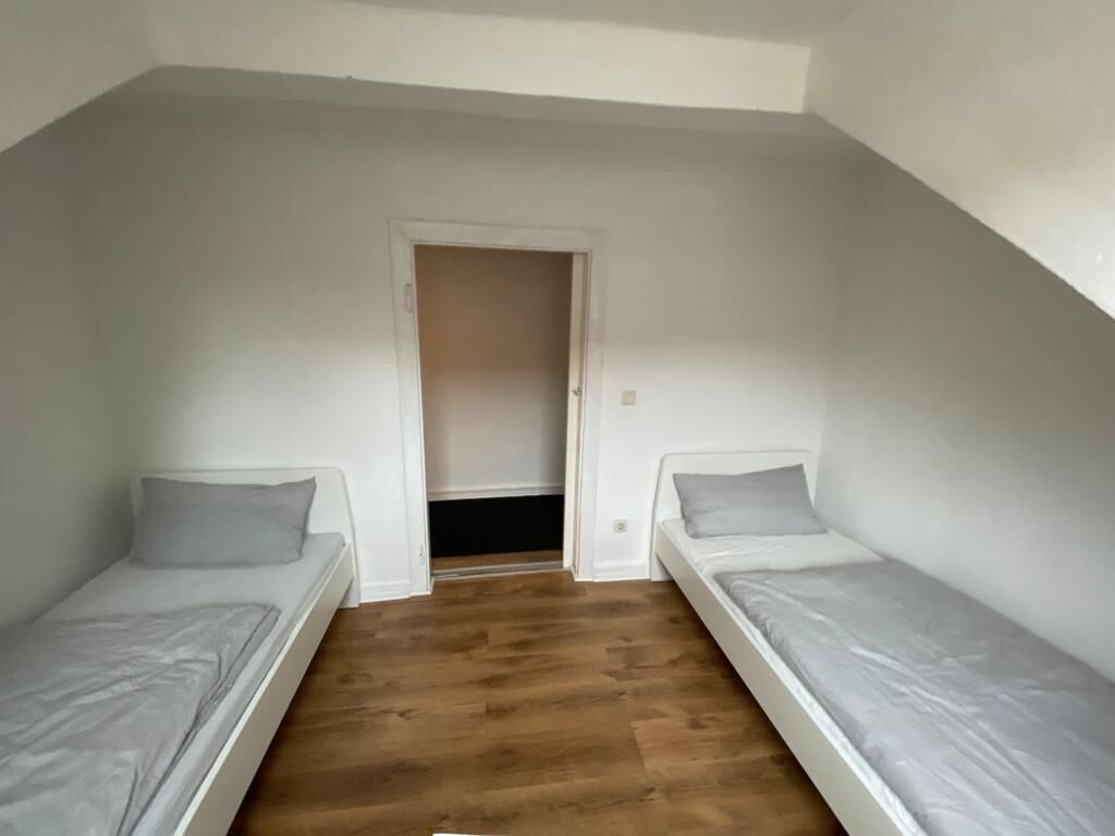 Um apartamento pequeno, de um quarto, com duas camas de solteiro, piso de madeira e uma porta que dá para um armário.