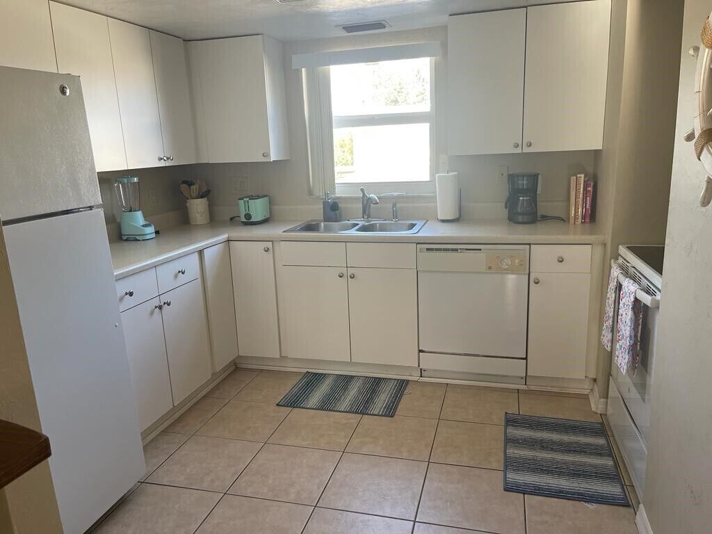 Una cocina con alacenas blancas, un refrigerador, un lavamanos, un lavavajillas, una ventana y una estufa.