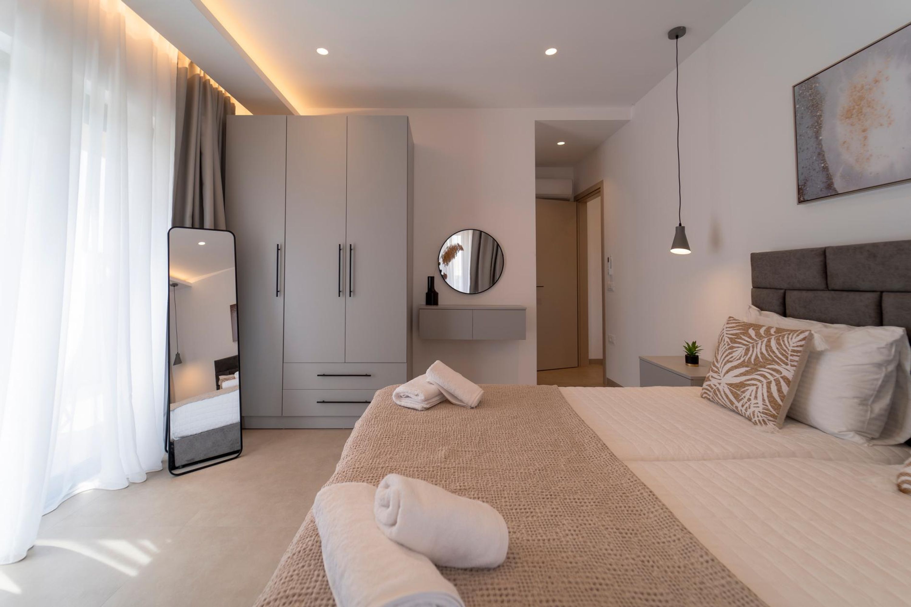 A modern bedroom with a large bed, a bedside table with a lamp, a wardrobe, and a mirror.