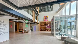 Un hall d’entrée spacieux avec un plafond haut, un mur de verre offrant une vue dégagée et une exposition d’œuvres d’art aux couleurs vives.