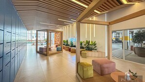 Un hall d’hôtel moderne avec un long couloir, des casiers, des espaces de détente et de grandes fenêtres.