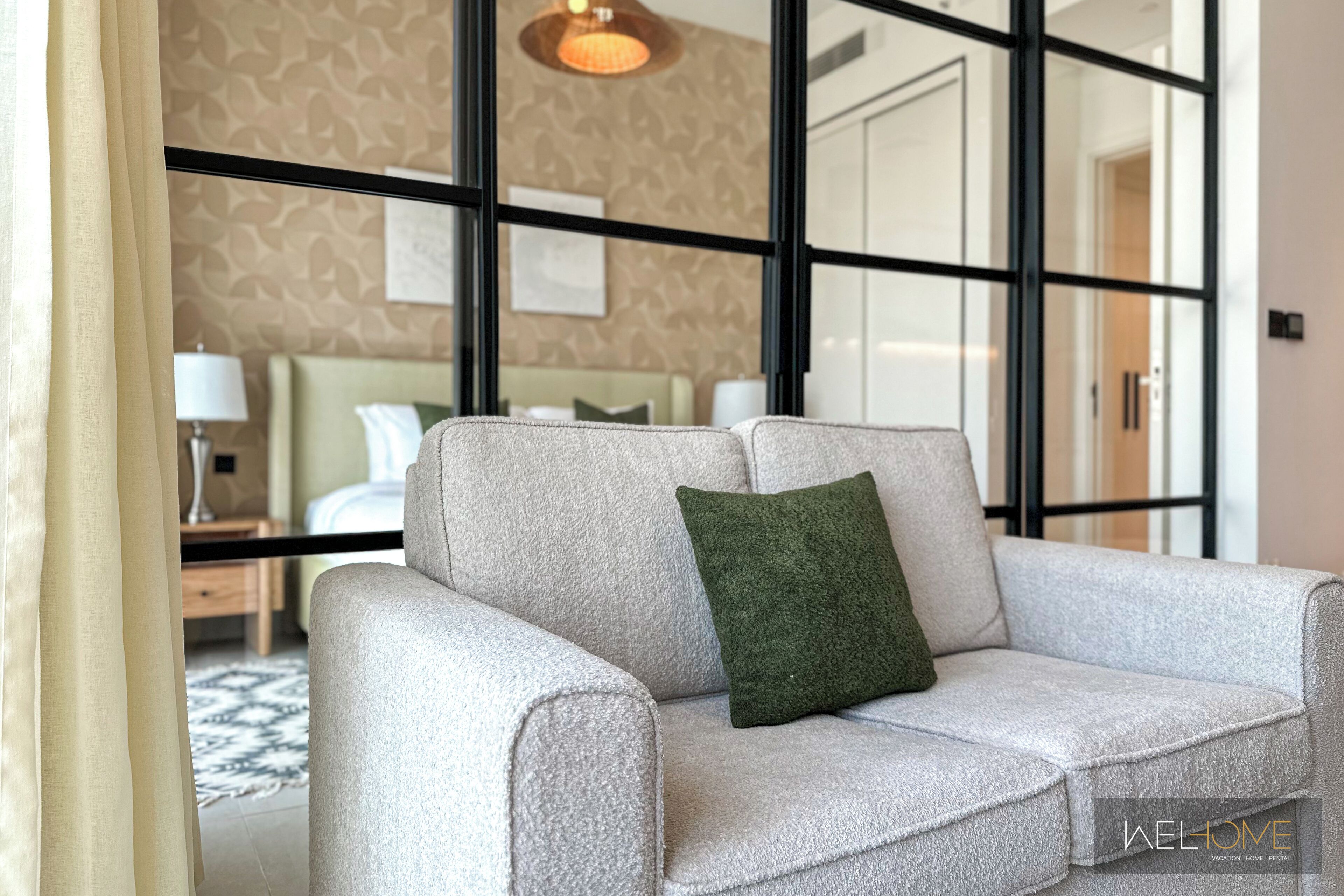 Een moderne hotelkamer met een grijze bank, een groen kussen en een behang met patroon.
