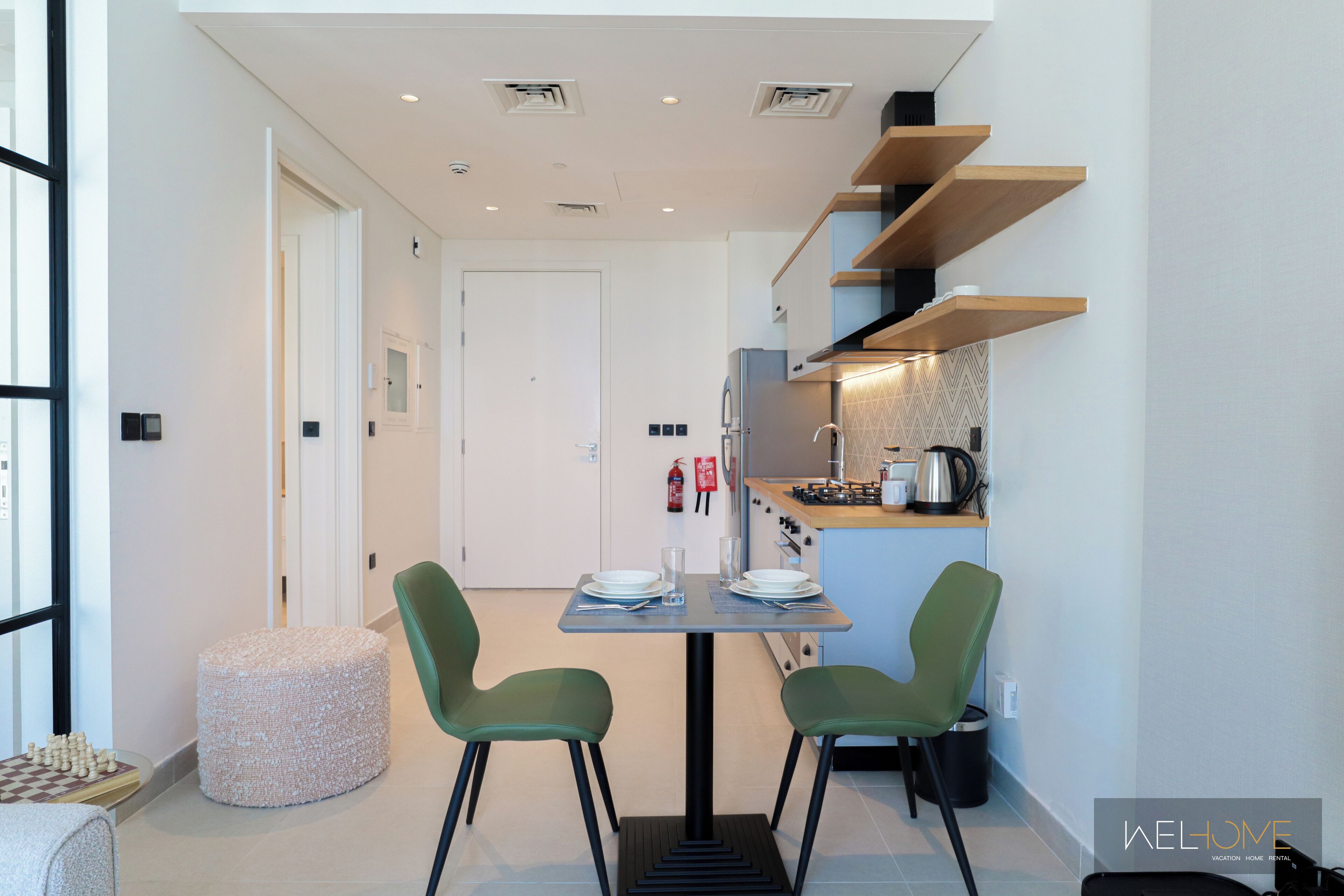 A compact kitchen with modern appliances, a dining area with two chairs, and a small round ottoman.