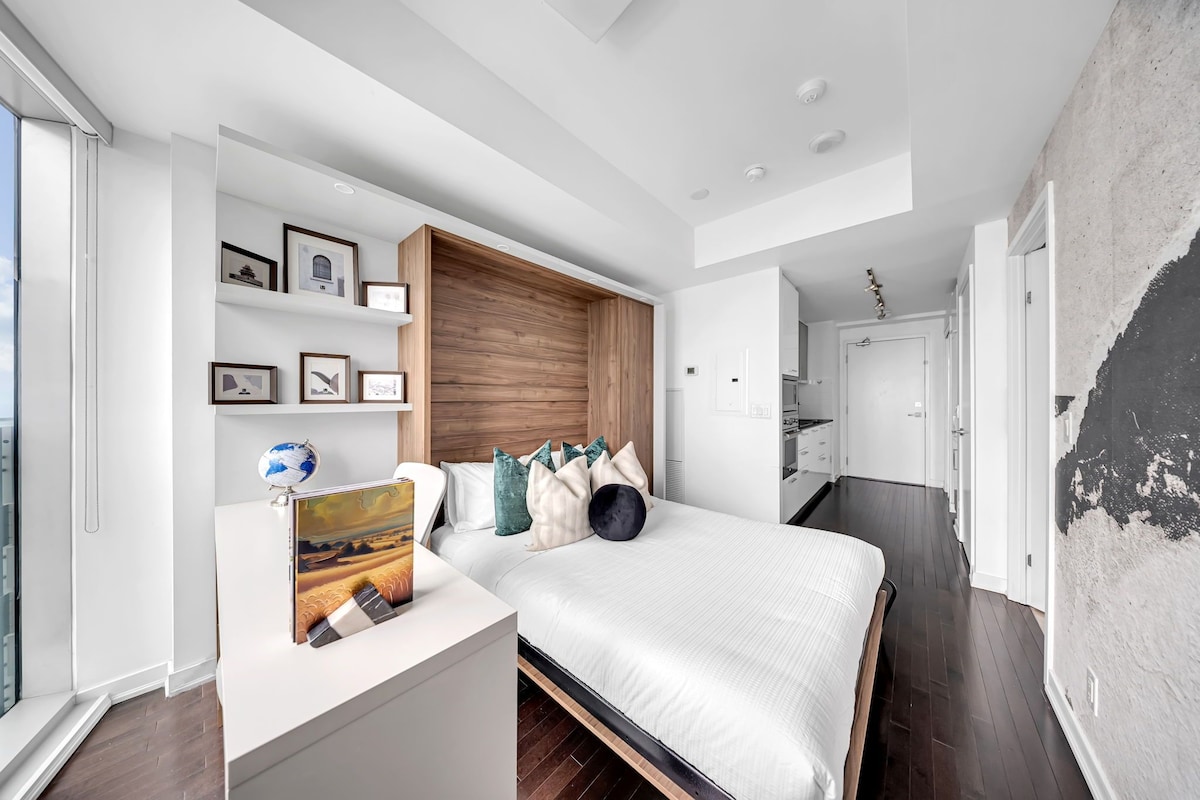 Un dormitorio moderno con una cama, mesitas de noche, un cabecero de madera y una pared decorada con marcos.
