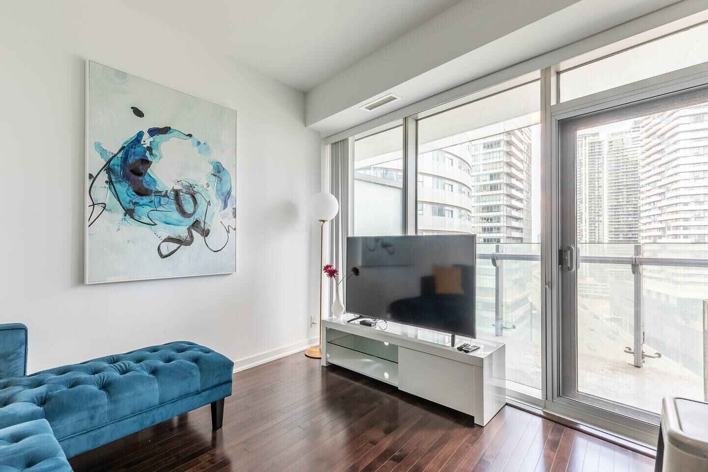A modern living room with a large window, a blue sofa, a flat-screen TV, and a contemporary abstract painting.