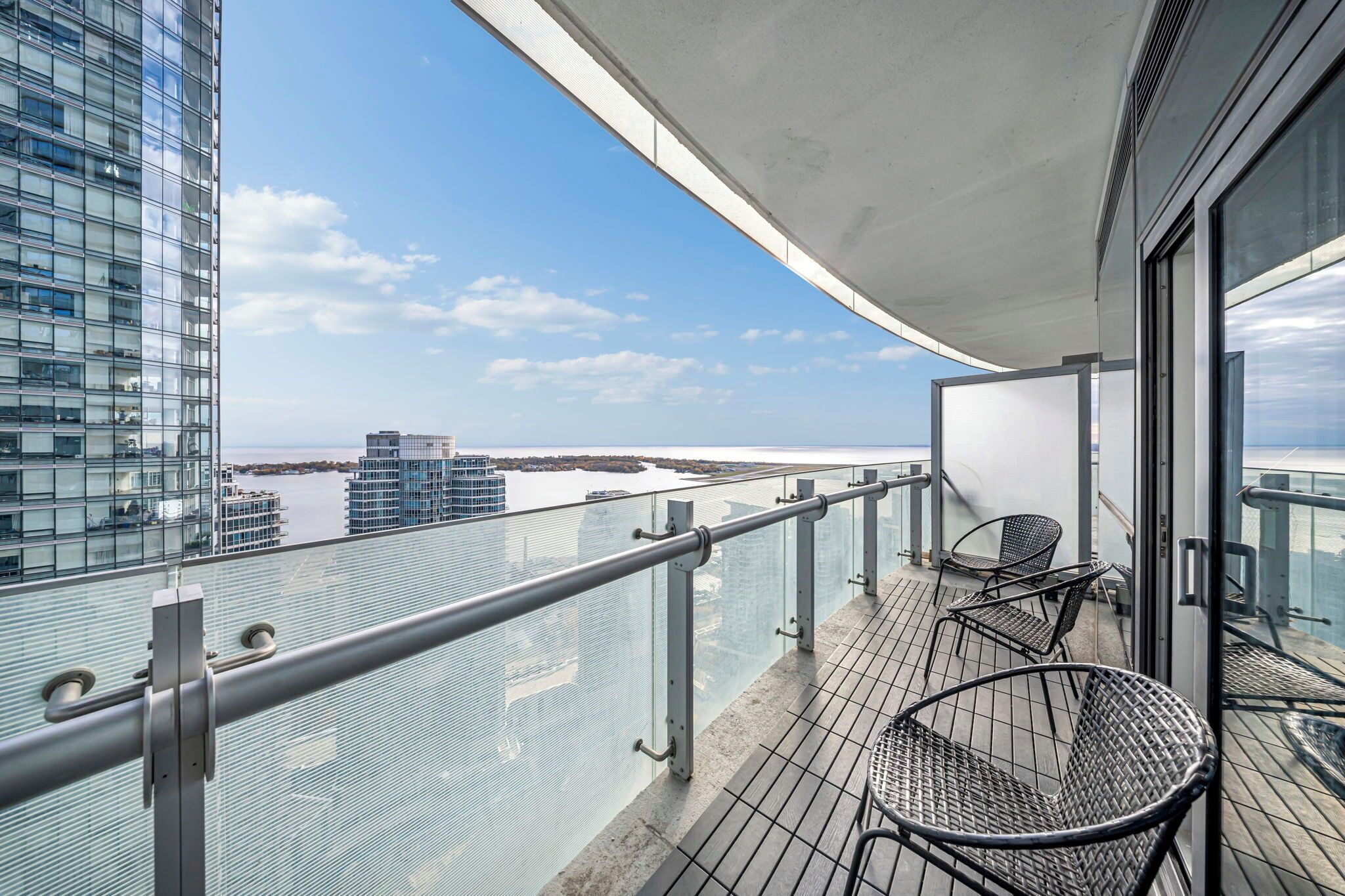 Ein Balkon mit Glasgeländer, der auf ein Gewässer und Gebäude blickt.
