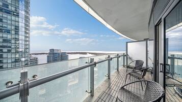 Ein Balkon mit Glasgeländer, der auf ein Gewässer und Gebäude blickt.