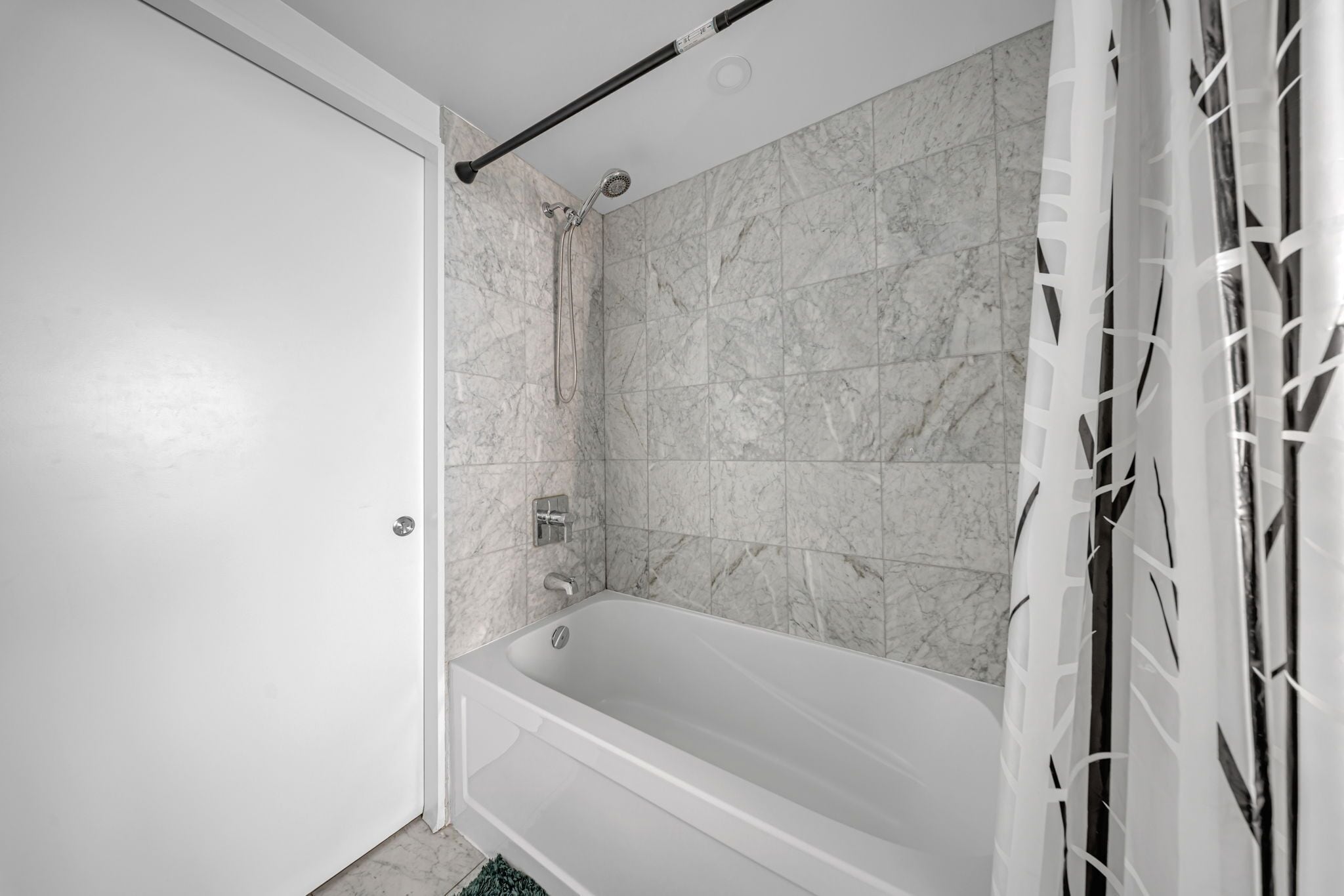 A bathroom with a bathtub, a shower, and a toilet. The walls are tiled with a marble-like pattern.
