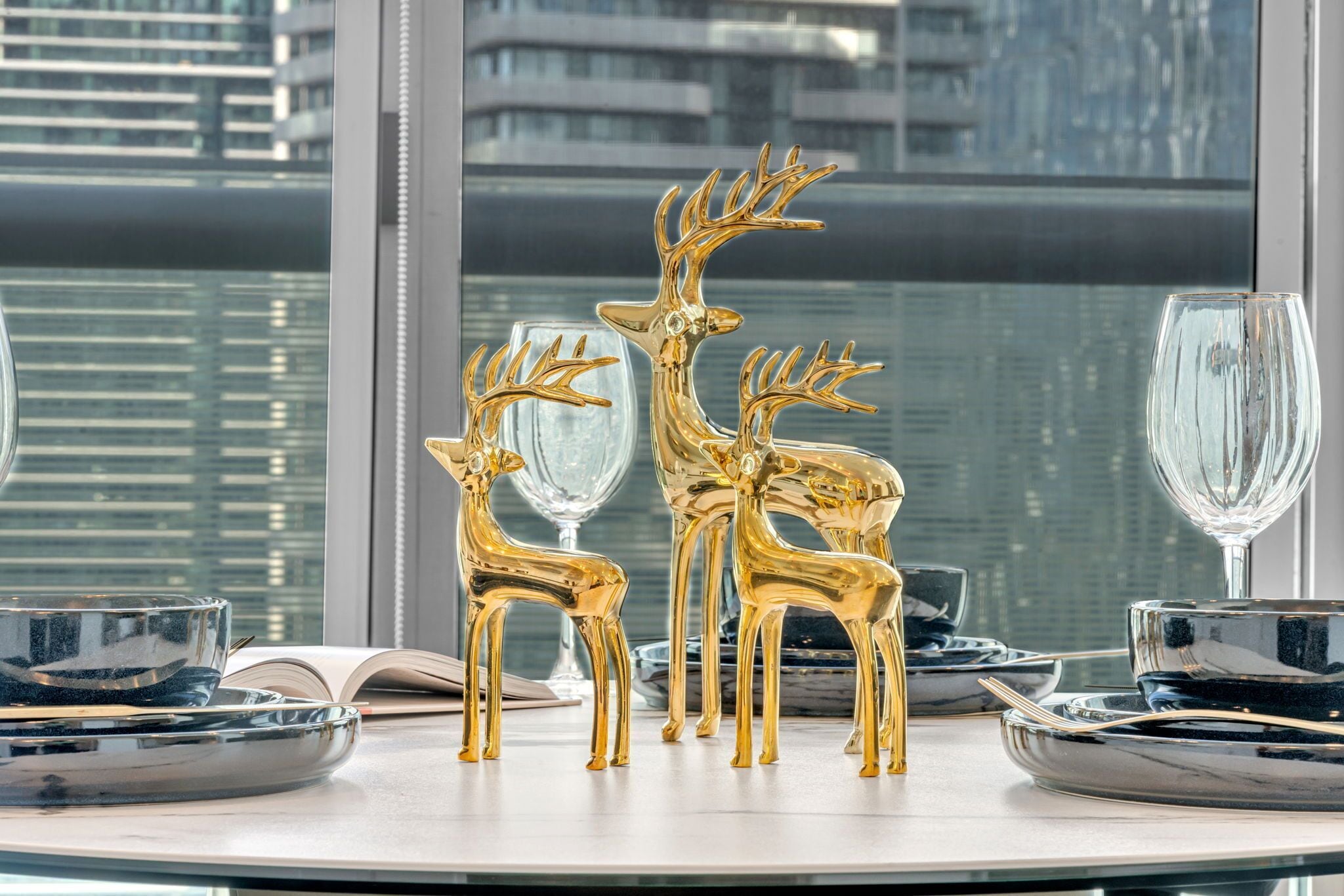 A table set with gold deer figurines, clear glassware, and black plates.