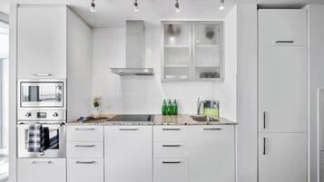 A modern kitchen with white cabinets, a built-in oven, a stove, and a microwave. There are three overhead lights and a window above the sink.