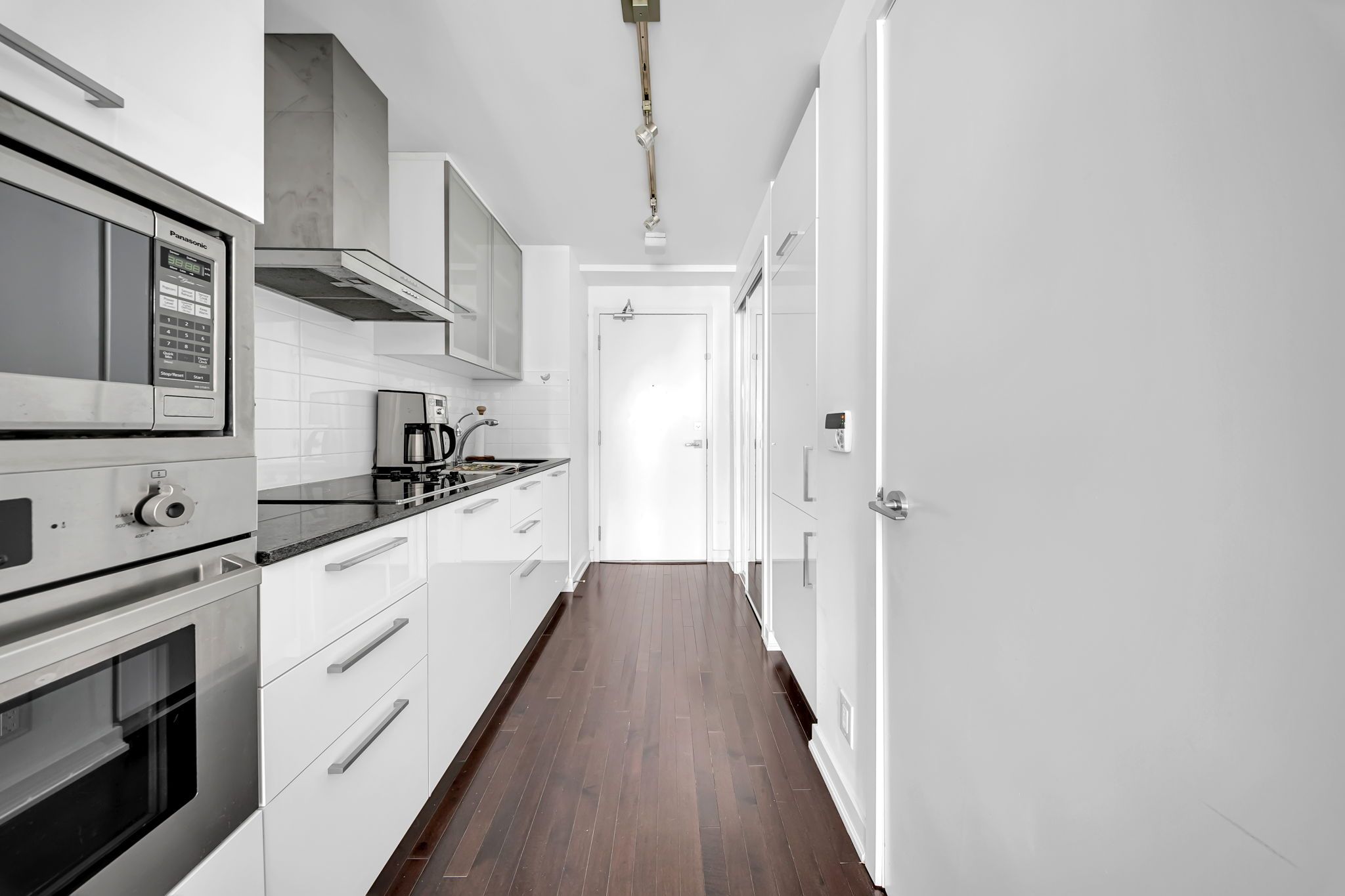 A modern kitchen with white cabinetry, a built-in oven, a coffee maker, and a stainless steel range hood.
