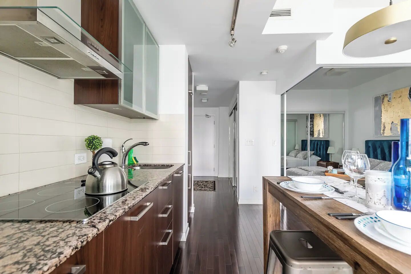 A modern kitchen with a granite countertop, stainless steel appliances, and a wooden dining area with a glass table.