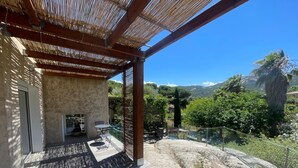 Um espaço coberto ao ar livre com uma mesa e cadeiras, um muro de pedra e vista para uma paisagem montanhosa.