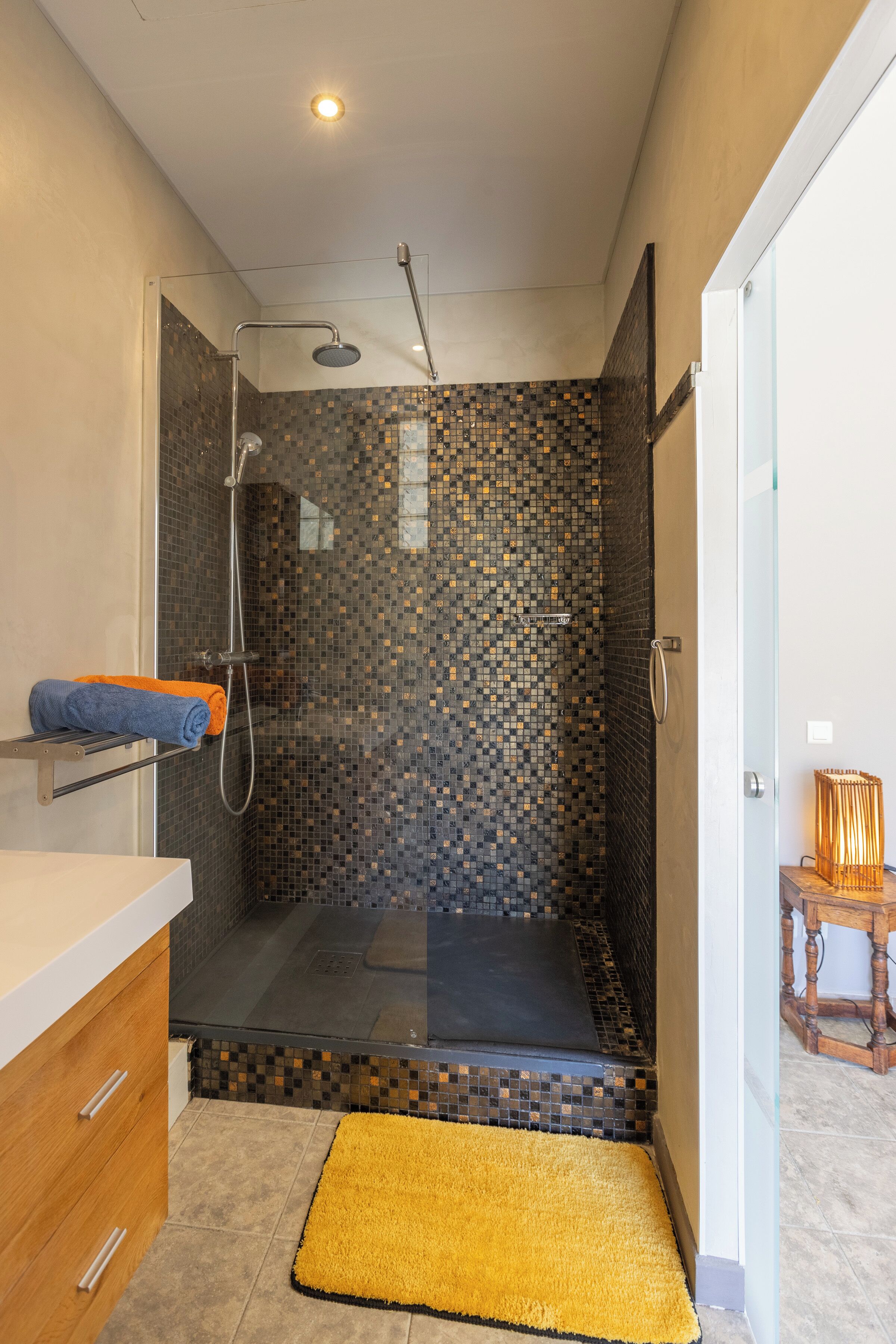 A modern bathroom with a shower area, a glass door, and a yellow rug.