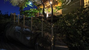 Escadaria externa iluminada com luzes de fada, cercada por pedras e vegetação.