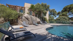 Área da piscina com espreguiçadeiras e deck de madeira.