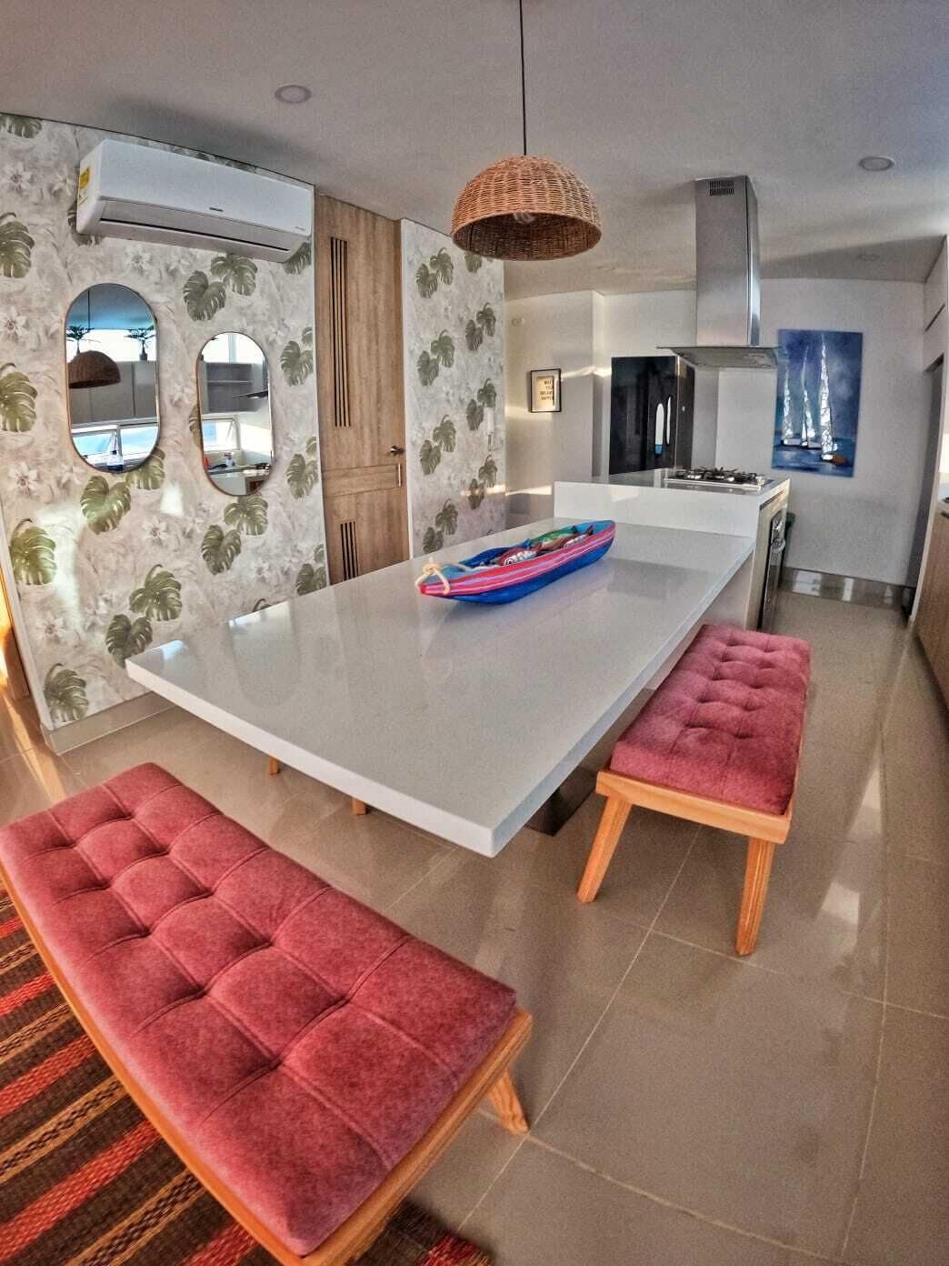 A modern kitchen with a central island, a dining area with red upholstered benches, and a hanging wicker light fixture.