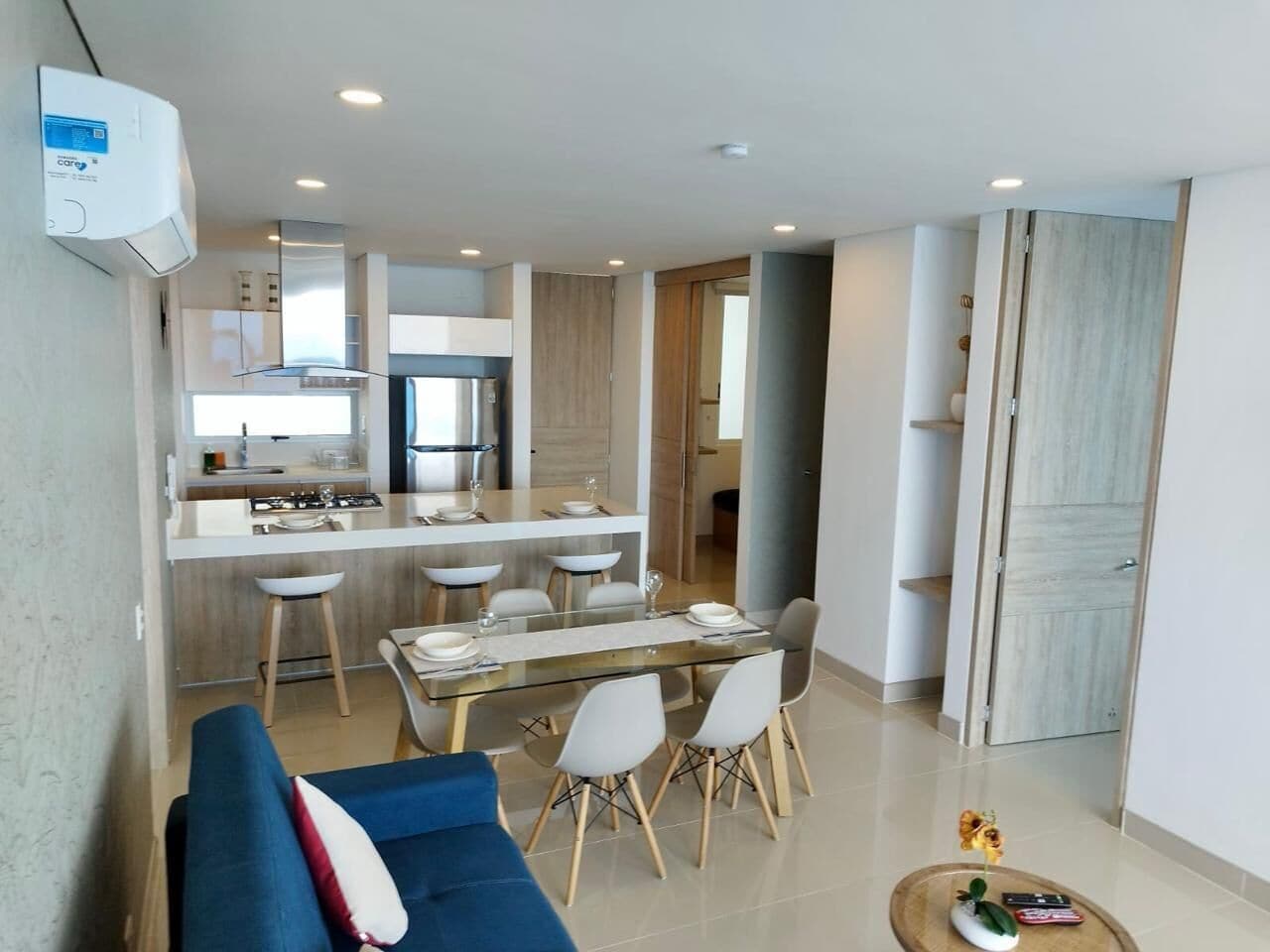 A modern apartment with a dining area, kitchen, and a living room with a sofa and coffee table.