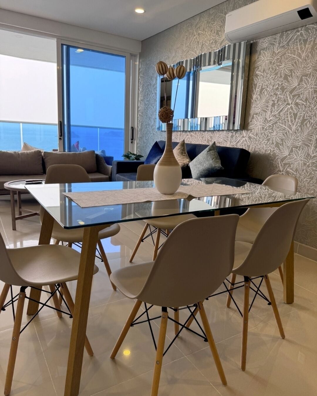 A modern dining area with a glass table, wooden chairs, and a vase with decorative items.