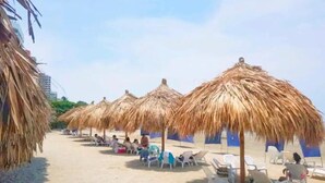 A beach with thatched umbrellas and white lounge chairs. - Reserva del Mar Apartamentos (Santa Marta)