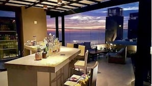A modern kitchen with a bar area, large windows, and a view of the city skyline at sunset. - Reserva del Mar Apartamentos (Santa Marta)